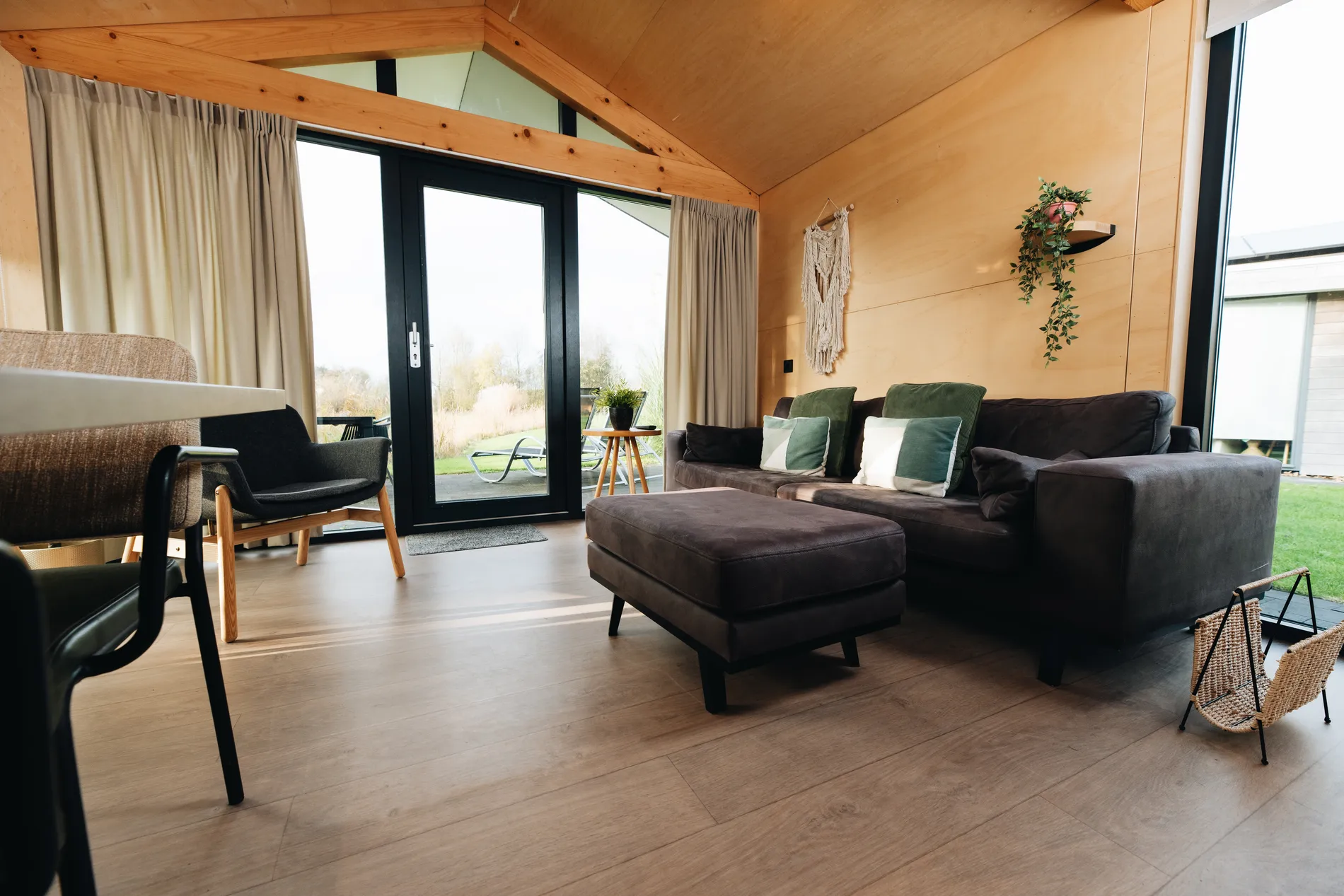 Sfeervolle woonkamer van een houten vakantiewoning bij Resort Land & Zee met een donkere bank, houten wanden en uitzicht op de natuur.